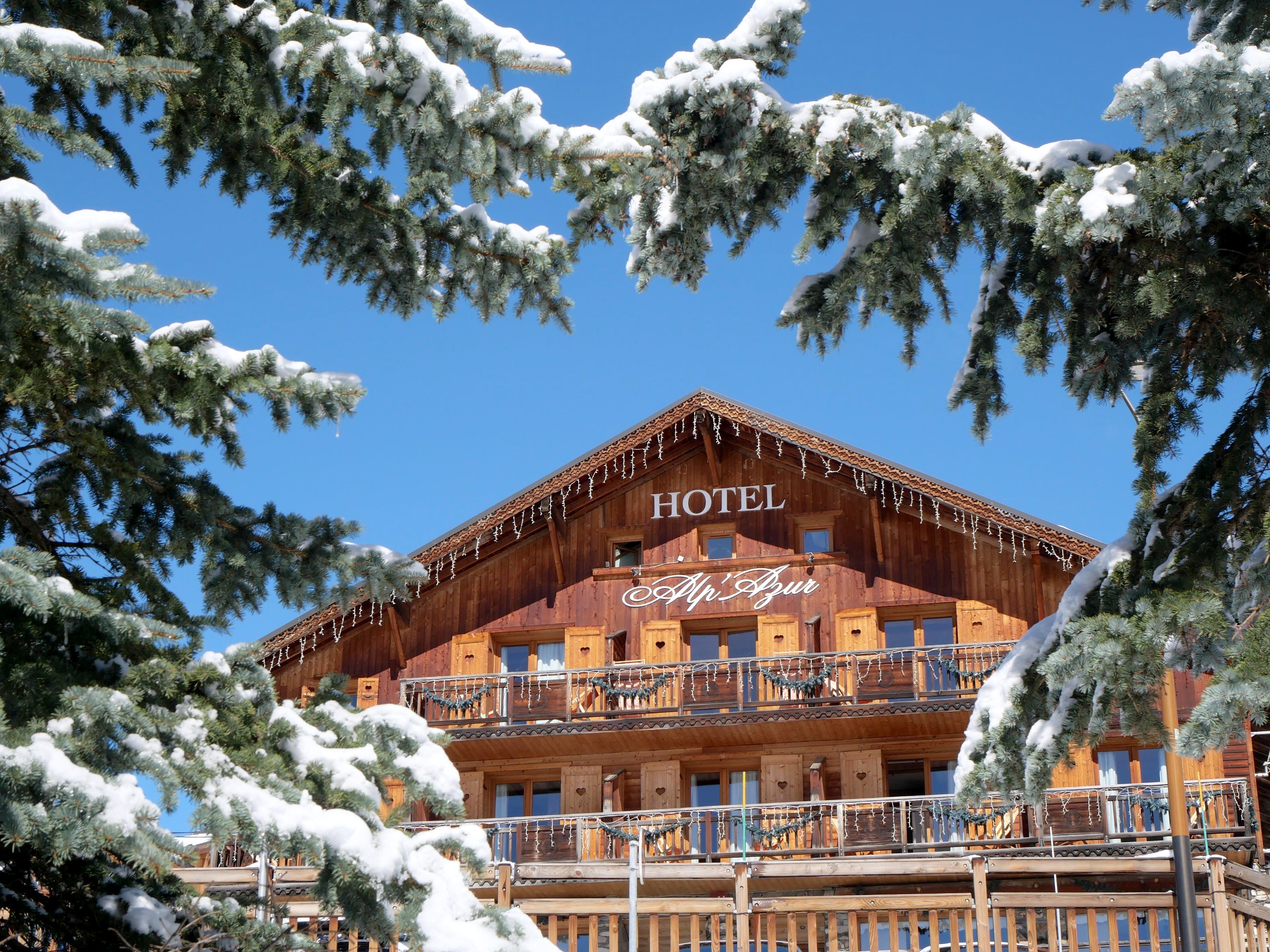 L'Hôtel Alp'Azur en hiver, sous le ciel bleu et les sapins enneigés