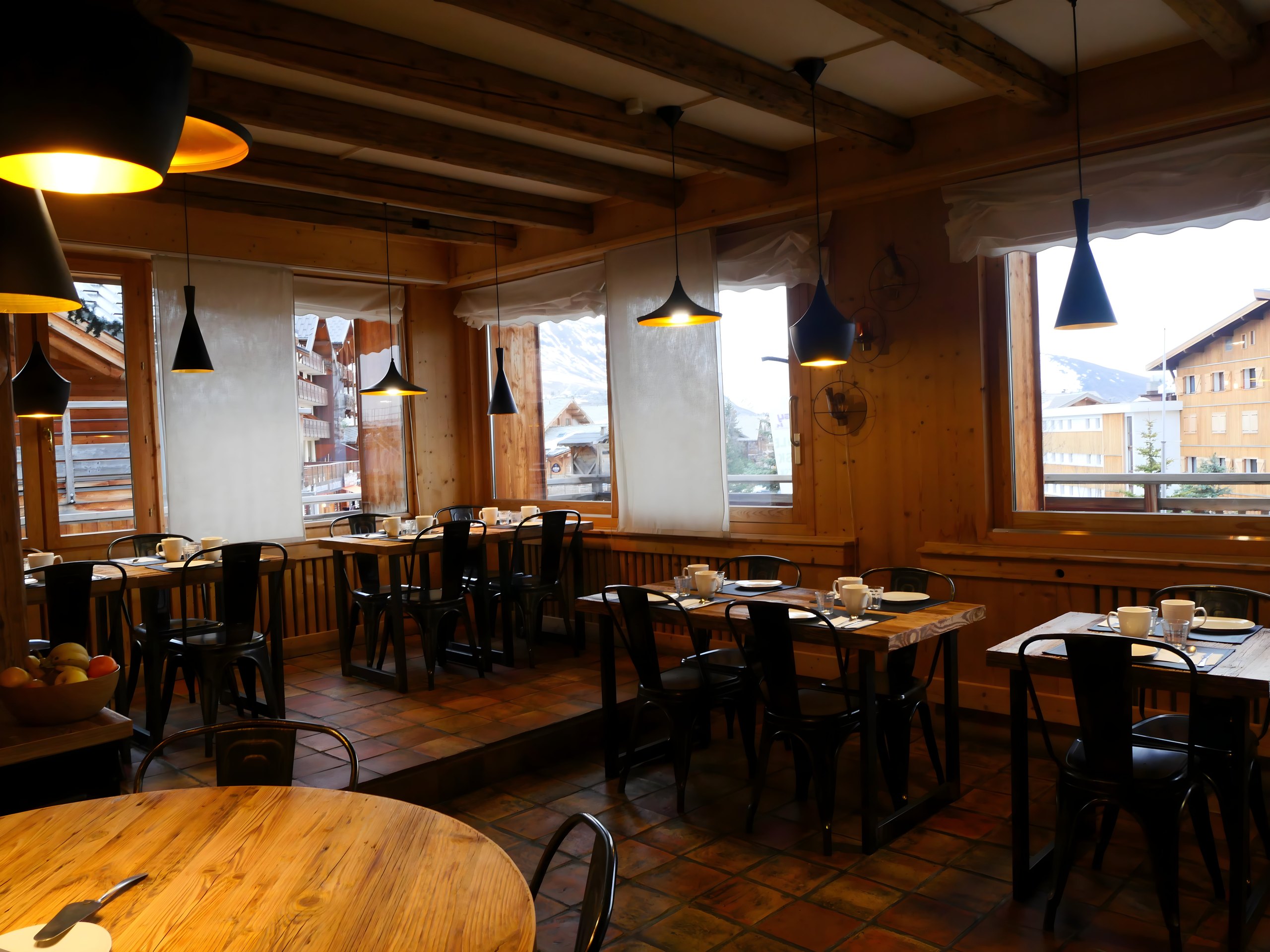 Salle du petit-déjeuner : boiseries, suspensions et vue sur la station